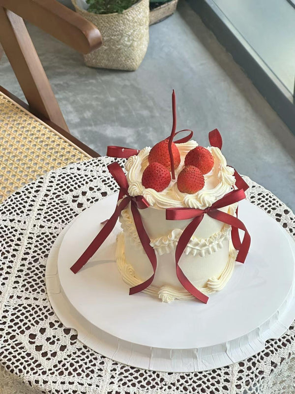 Light yellow cake decorated with red silk bow and strawberries